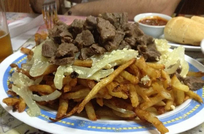 Gran plato de chorrillana chilena con papas fritas doradas, cubiertas con cebolla frita, huevo revuelto y trozos de carne de vacuno.