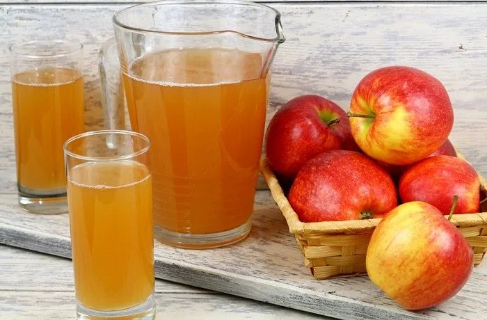 Chicha de manzana chilena Jarra de vidrio con chicha de manzana artesanal chilena, de color amarillo dorado, con manzanas frescas al fondo.
