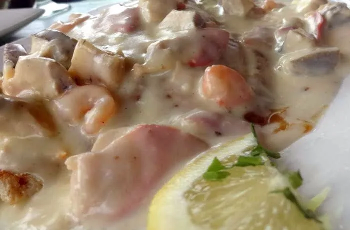 Congrio en salsa margarita Medallón de congrio chileno bañado en una espesa salsa blanca con choritos, machas y camarones visibles.