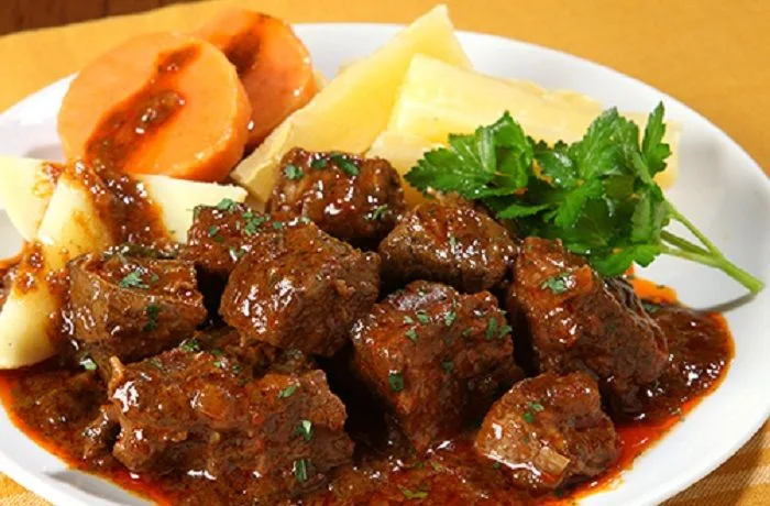 Watia o huatia chilena Plato de watia o huatia chilena, un guiso de carne de res tierno acompañado de papas cocidas y decorado con hierbas frescas.