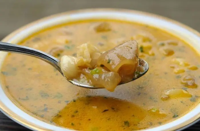 Caldo de pata de vacuno chileno (sopa de res) con trozos de pata y sémola, servido en un plato hondo con cilantro picado.
