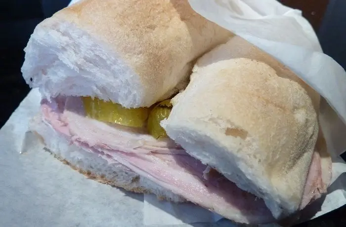 Sándwich de arrollado de malaya Un sándwich de malaya en marraqueta con anillos de ají verde sobre una tabla de madera.