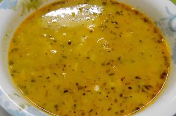 Caldo de harina tostada Un tazón de sopa de harina tostada humeante, con hilos de huevo blanco y un toque de merkén rojo en la superficie.