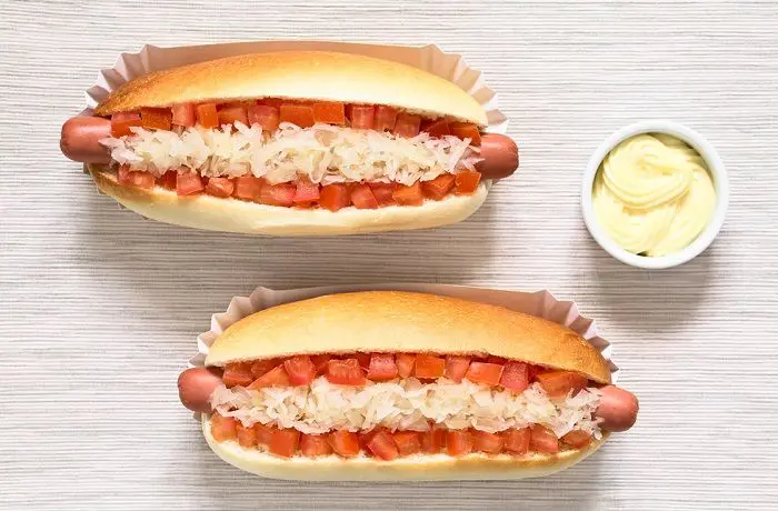 Dos completos chilenos con vienesa, tomate, chucrut y mayonesa, servidos en una tabla.