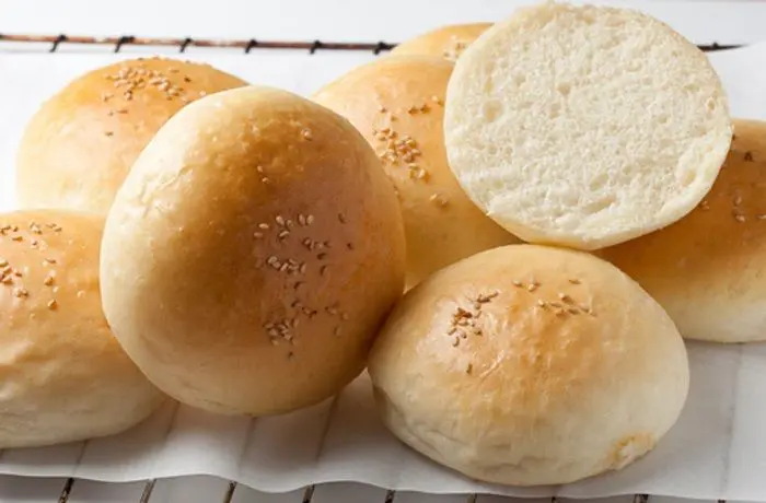 Pan de hamburguesa Un pan frica o de hamburguesa con su característica corteza dorada y miga suave, abierto y listo para ser tostado y rellenado.
