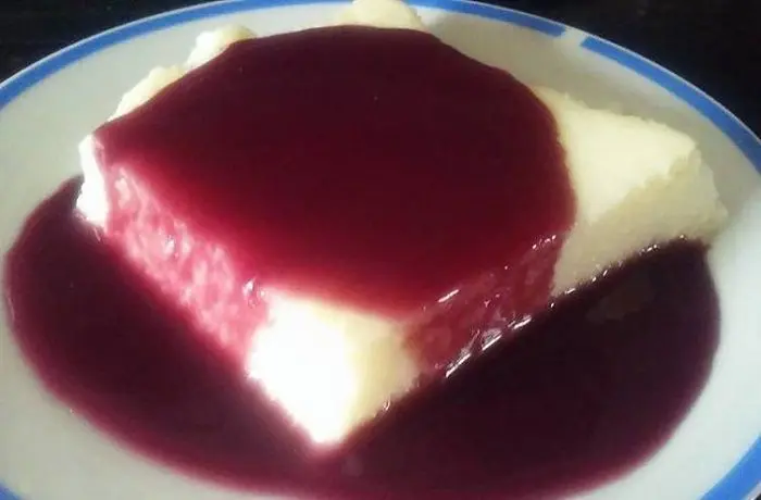 Sémola con salsa de vino tinto Porción de sémola con leche de color crema, bañada generosamente con una salsa de vino tinto brillante y oscura.
