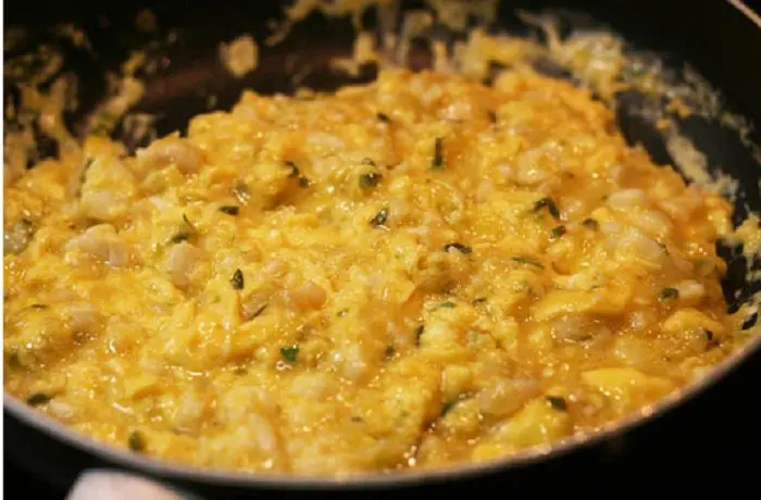 Revuelto de merluza desmenuzada con huevos, perejil y merkén, servido caliente en una sartén. Plato típico de caleta chilena.