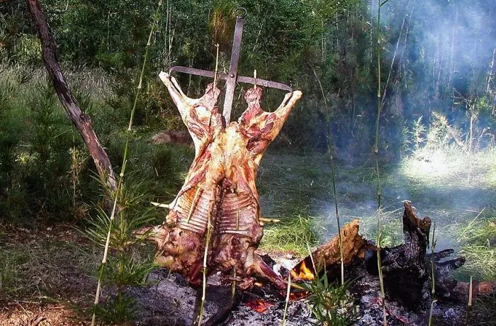 Cordero al palo Cordero entero asándose lentamente al estilo chileno sobre brasas, fijo a una estructura metálica o "palo".