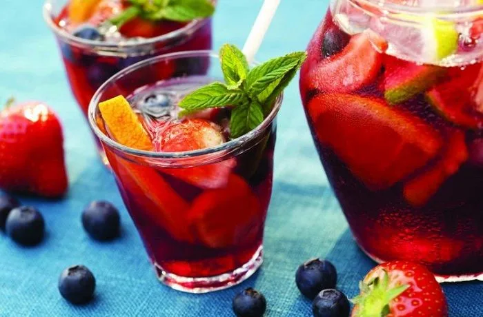 Sangría a la chilena en jarra con frutas flotando, servida con hielo.
