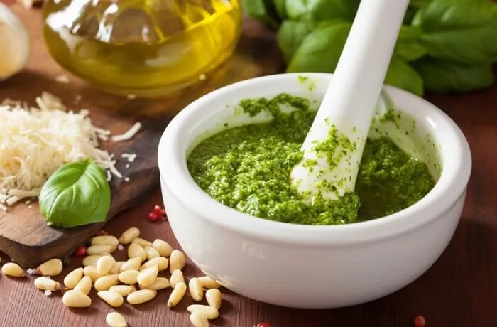 Salsa pesto tradicional Salsa pesto de albahaca tradicional, verde brillante, servida en un tazón blanco con ingredientes frescos alrededor.