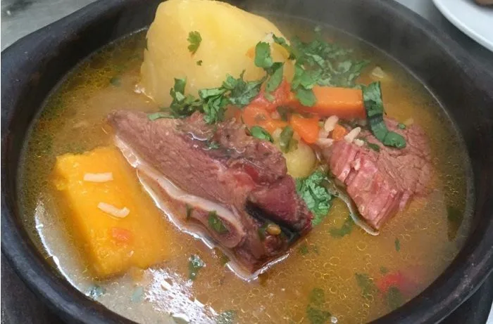 Receta de cazuela de chancho ahumado: Un clásico del sur de Chile 1 Cazuela de chancho ahumado chilena servida en plato de greda con un trozo de costillar, verduras y cilantro fresco.