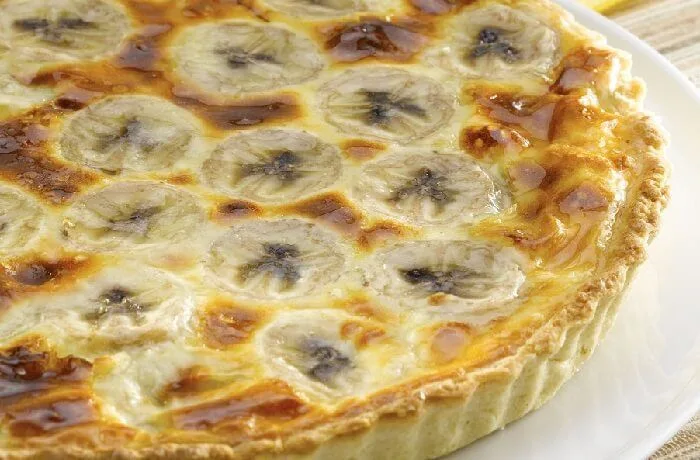 Kuchen de plátano casero, recién horneado y decorado, servido en una mesa rústica.