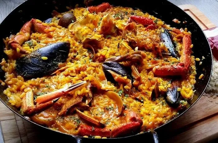 Receta de paella de mariscos española: Un emblema gastronómico europeo 1 Una paellera rebosante de arroz amarillo intenso, decorada simétricamente con camarones grandes, choritos en su concha y tiras de pimiento rojo.