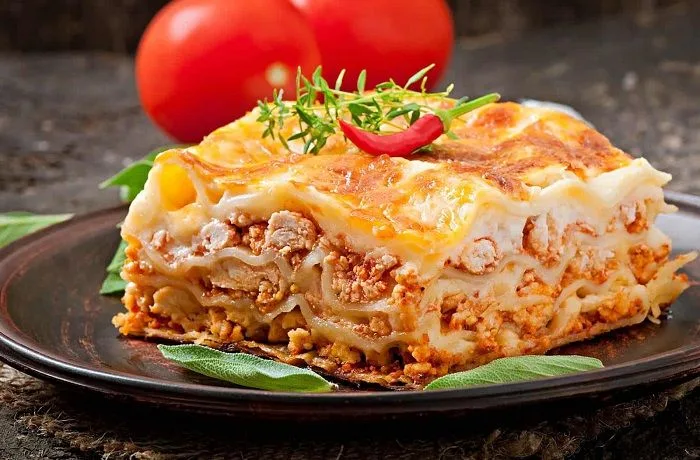 Receta de lasaña boloñesa casera: Clásico familiar italiano original 1 Una porción de lasaña tradicional servida en un plato blanco, mostrando capas de pasta, carne con tomate y queso fundido gratinado.