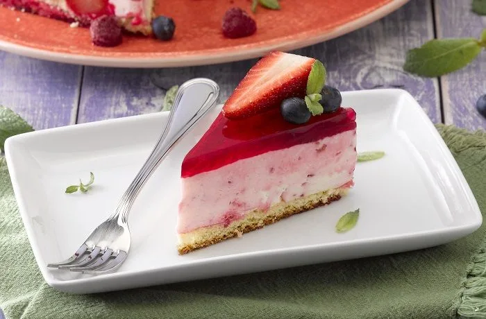 Receta de torta de yogurt y bizcocho - Comidas Chilenas Torta de yogurt y bizcocho con una capa superior de gelatina roja vibrante y frutillas frescas en el interior.