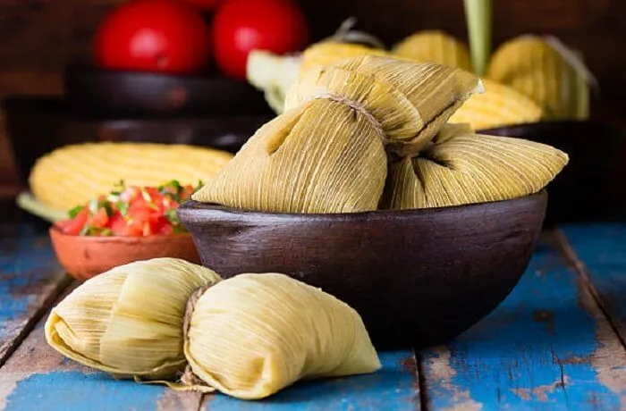 Humitas de choclo chilenas: Pasta cremosa de maíz y albahaca envuelta en hojas de choclo, cocida y lista para servir.