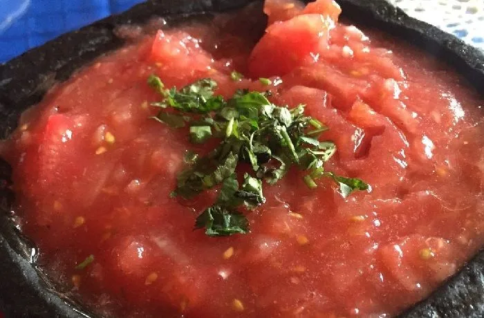 Chancho en piedra chileno preparado en un mortero de piedra tradicional con tomates y ají verde.