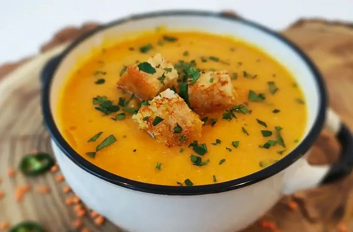 Receta de crema de lentejas casera: Comida reconfortante de aprovechamiento 1 Plato hondo con crema de lentejas de color ocre suave, decorada con cilantro fresco picado y crutones dorados.