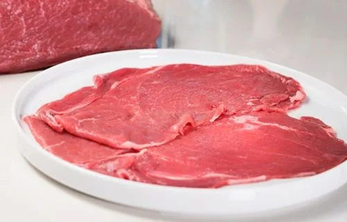 Láminas finas de carne de res siendo selladas en una sartén caliente hasta quedar doradas y jugosas.