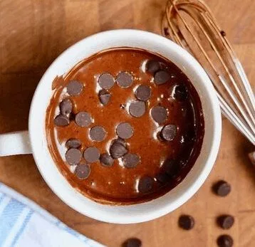 Chispas de chocolate siendo añadidas sobre la mezcla de queque en una taza.