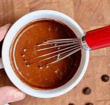 Masa de queque en taza de color chocolate siendo mezclada en un bol.