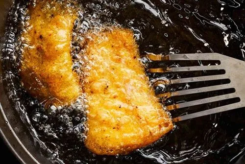 Freír el pescado Pescado blanco rebozado friéndose en aceite caliente, mostrando una cubierta dorada y burbujeante.