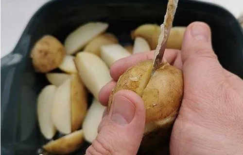 Preparando las papas para el horno Gajos de papas sumergidos en una mezcla de aceite de oliva, ajo picado y especias en un bol de vidrio.