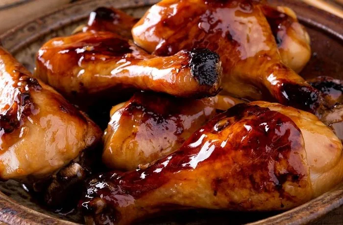 Receta de pollo a la Coca-Cola: Tradicional preparación cantonesa 1 Presas de pollo bañadas en un glaseado oscuro y brillante de Coca-Cola, servidas en una fuente con una textura suave y caramelizada.