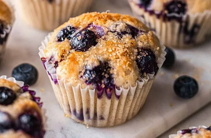 Muffins de arándanos recién horneados con arándanos frescos visibles en la superficie dorada.