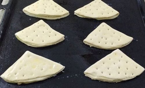 Dobladitas en bandeja de horno Dobladitas dobladas en forma triangular, pinceladas con huevo, sobre una lata de horno.