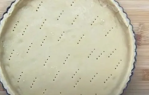 Masa de kuchen distribuida en un molde redondo y engrasado, lista para rellenar.