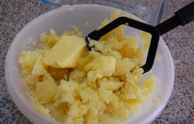 Papas cocidas siendo molidas rústicamente con una cuchara de madera en la olla.