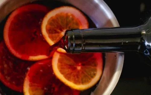 Añadiendo el vino Rodajas de naranja fresca, canela entera y clavos de olor infusionándose en vino tinto a fuego bajo.