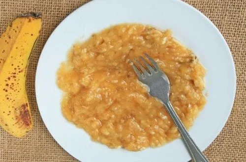 Platano molido Un plato con un plátano maduro machacado con tenedor hasta formar un puré suave y homogéneo.