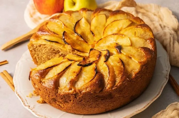 ¿Cómo hacer queque de manzana? Receta casera, esponjosa y fácil de preparar 1 Un queque de manzana chileno recién horneado y espolvoreado con azúcar flor, decorado con láminas de manzana doradas en la parte superior.