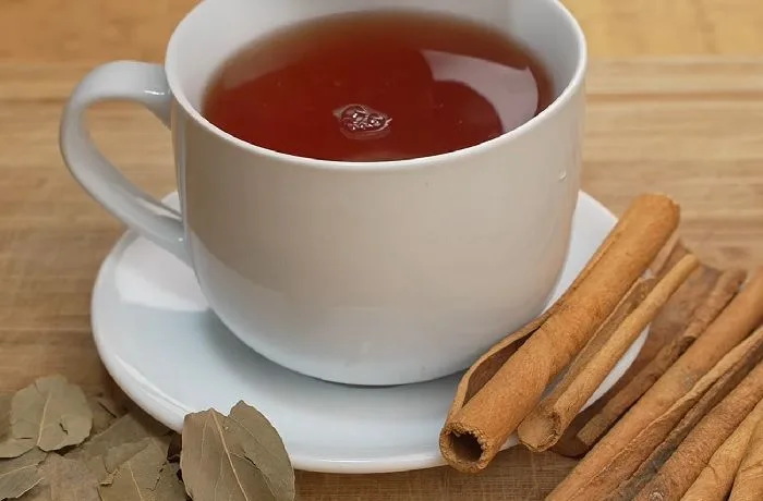 Receta de té japonés para bajar de peso y disminuir la hinchazón 1 Taza de té japonés caliente de color dorado, preparado con hojas de laurel y canela, con un gajo de limón al lado.