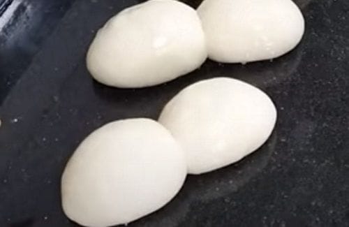Bollos de marraqueta Porciones de masa de marraqueta ovilladas en formas redondas y lisas, reposando sobre una superficie de acero inoxidable antes del formado final.