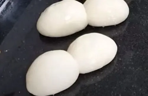 Bollos de marraqueta Porciones de masa de marraqueta ovilladas en formas redondas y lisas, reposando sobre una superficie de acero inoxidable antes del formado final.