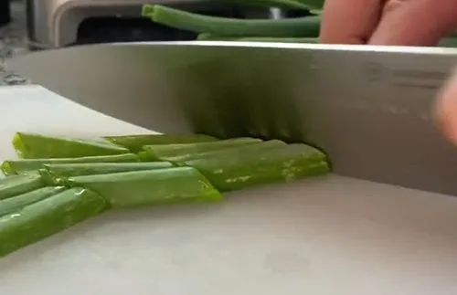 Tallos de cebollín fresco cortados finamente en rodajas diagonales, mostrando la transición del blanco del bulbo al verde intenso.