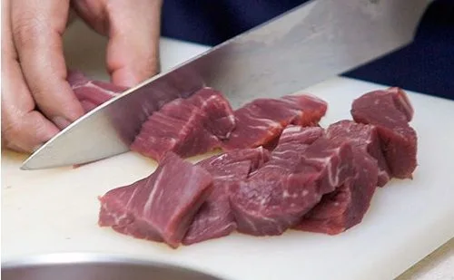 Carne en cubos Cubos de carne de res cruda siendo preparados para el proceso de marinado con especias y cítricos.