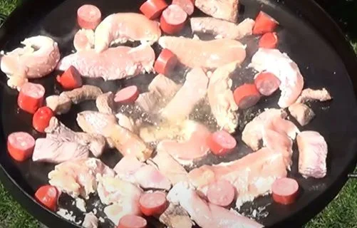 Cortes de plateada de cerdo, pollo y longaniza sellándose en el disco de arado con aceite caliente.