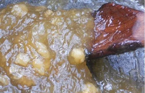 Una olla de acero con el dulce de alcayota hirviendo suavemente, adquiriendo su color dorado translúcido.