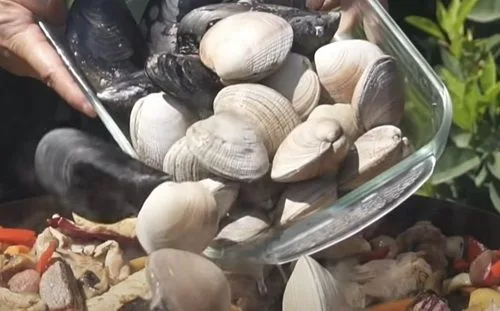 Almejas y choritos incorporándose al guiso de carnes y verduras en el disco de arado con vino blanco.