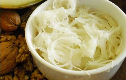 Fibras de alcayota crudas separadas con un tenedor junto a un bol de nueces picadas.