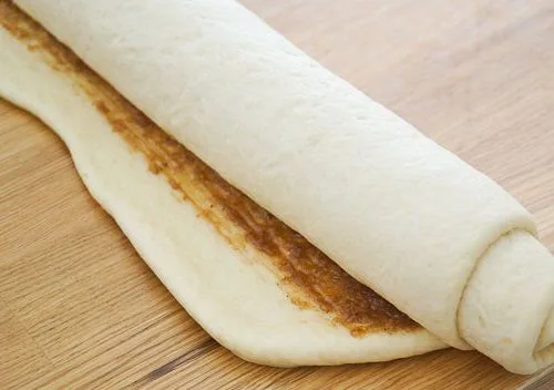 Masa de rollos de canela Un gran rectángulo de masa extendido, cubierto uniformemente con una pasta de azúcar rubia y canela antes de ser enrollado.