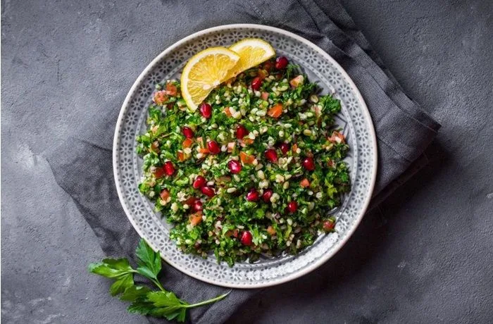 Ensalada de perejil árabe o tabule servida en un bol de madera con granada y limón.