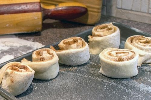 Rollos de canela al horno Doce piezas de rollitos alineadas en una fuente para horno, mostrando el crecimiento de la masa antes de entrar al calor.
