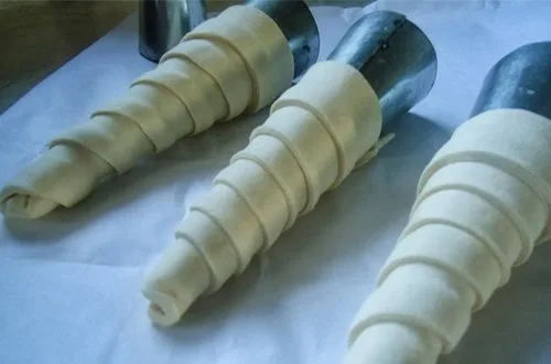 Cachitos envueltos Tiras de masa envueltas en moldes cónicos, listas para hornearse.