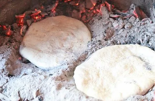 Tortillas de rescoldo cocinándose directamente sobre cenizas calientes de una fogata.