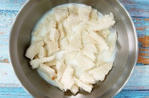 Pan remojado Pan marraqueta desmenuzado y remojándose en leche, paso clave para la textura cremosa del pastel.